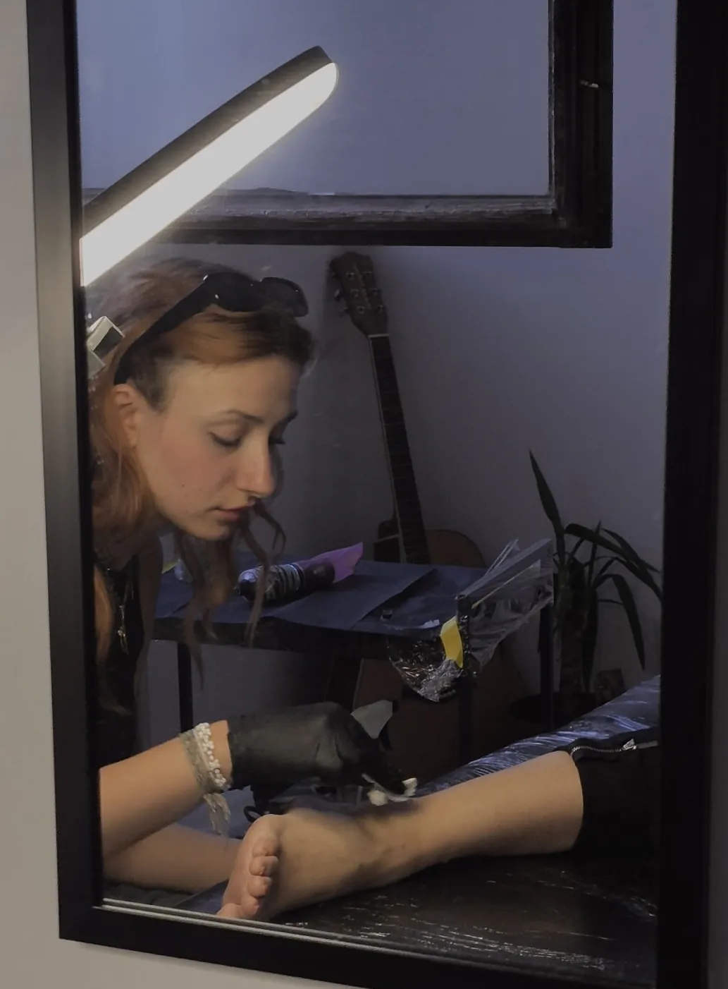 Jana tetovira u studiju, u crnim rukavicama, viđena u ogledalu